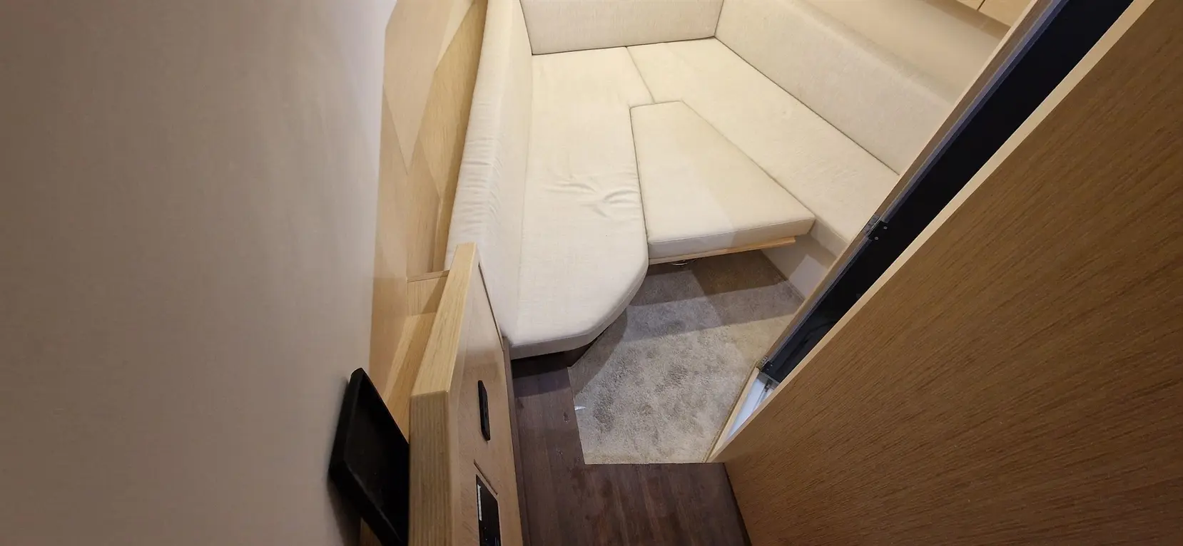 A compact room featuring a light-coloured sofa, wooden furniture, and a carpeted floor, with a door partially open.